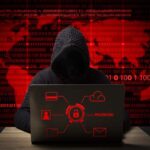 hacker in a jacket with a hood with a laptop sits at the table.