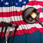 The judge’s hammer,the US flag, and an hourglass lie on a blue wooden table.