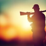 Male hunter silhouette with a gun at sunset